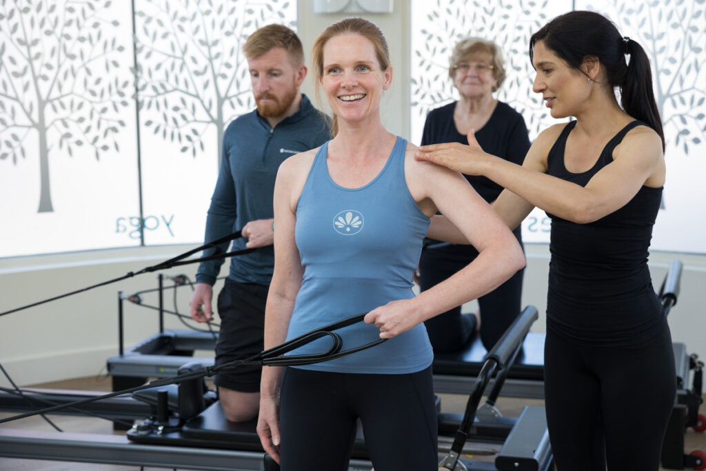 A lady smiling during a reformer pilates class. Health & Wellness Photography London