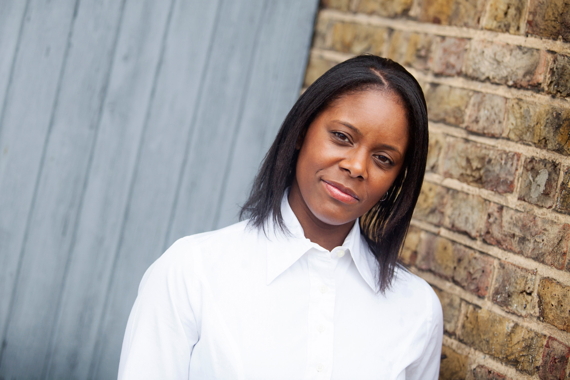London headshot photography, a business woman standing in front of a brick wall & blue wooden door.