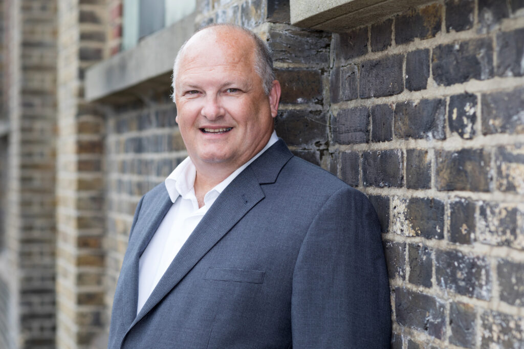 A man in a suit leans against a brick wall. Croydon headshot photography