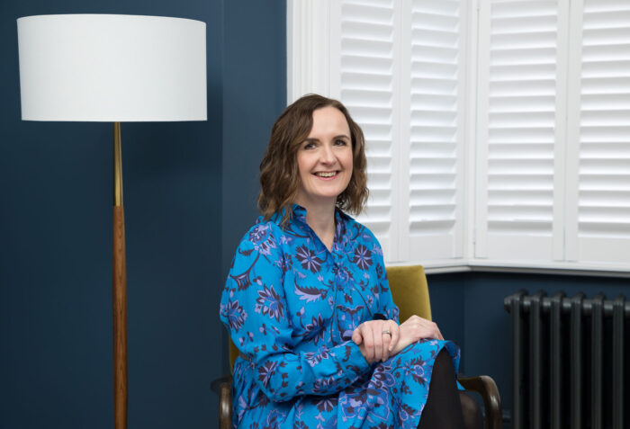 A personal branding photography image of a woman sitting in front of a blue wall in a Croydon house.