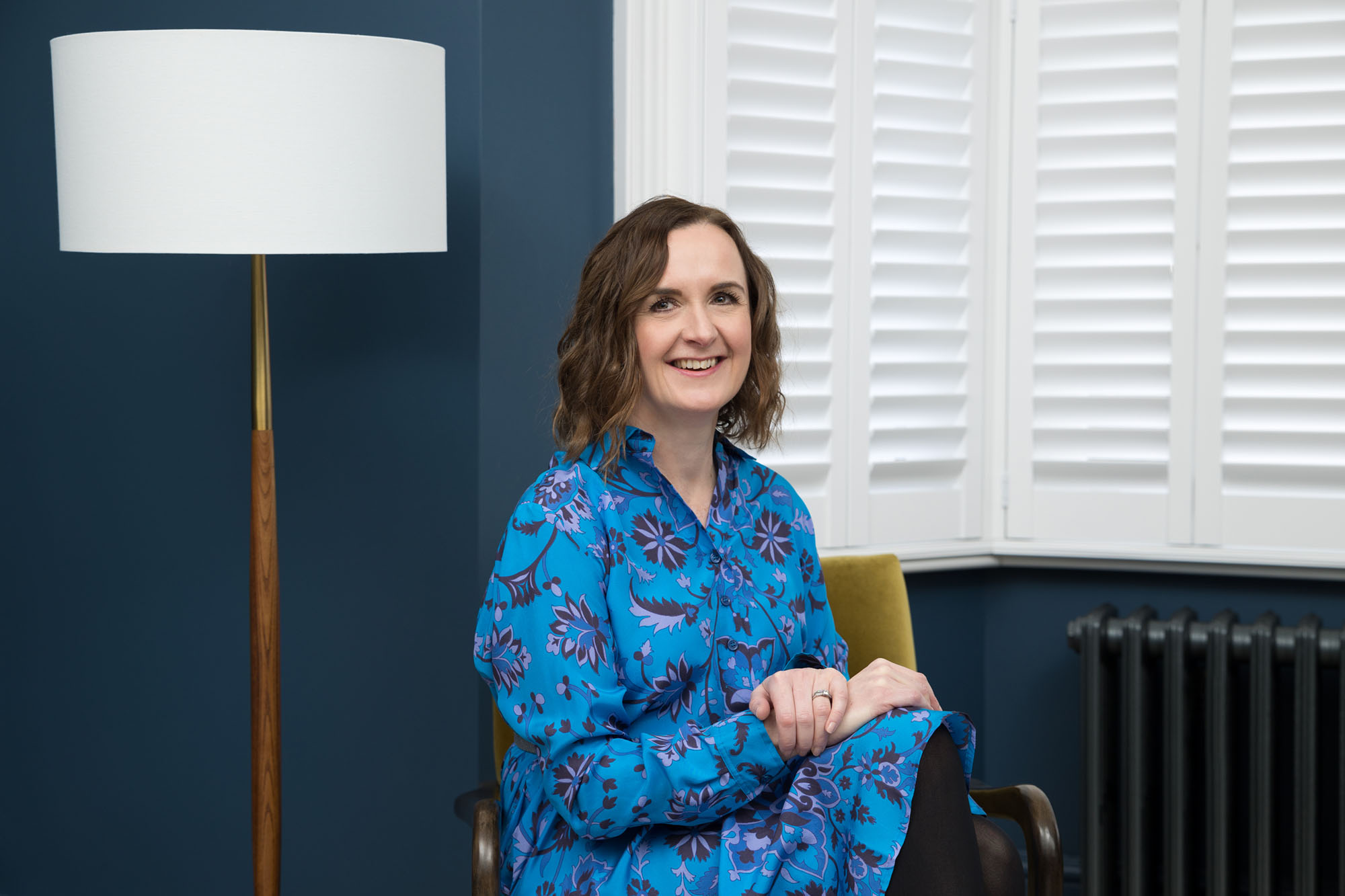 A personal branding photography image of a woman sitting in front of a blue wall in a Croydon house.