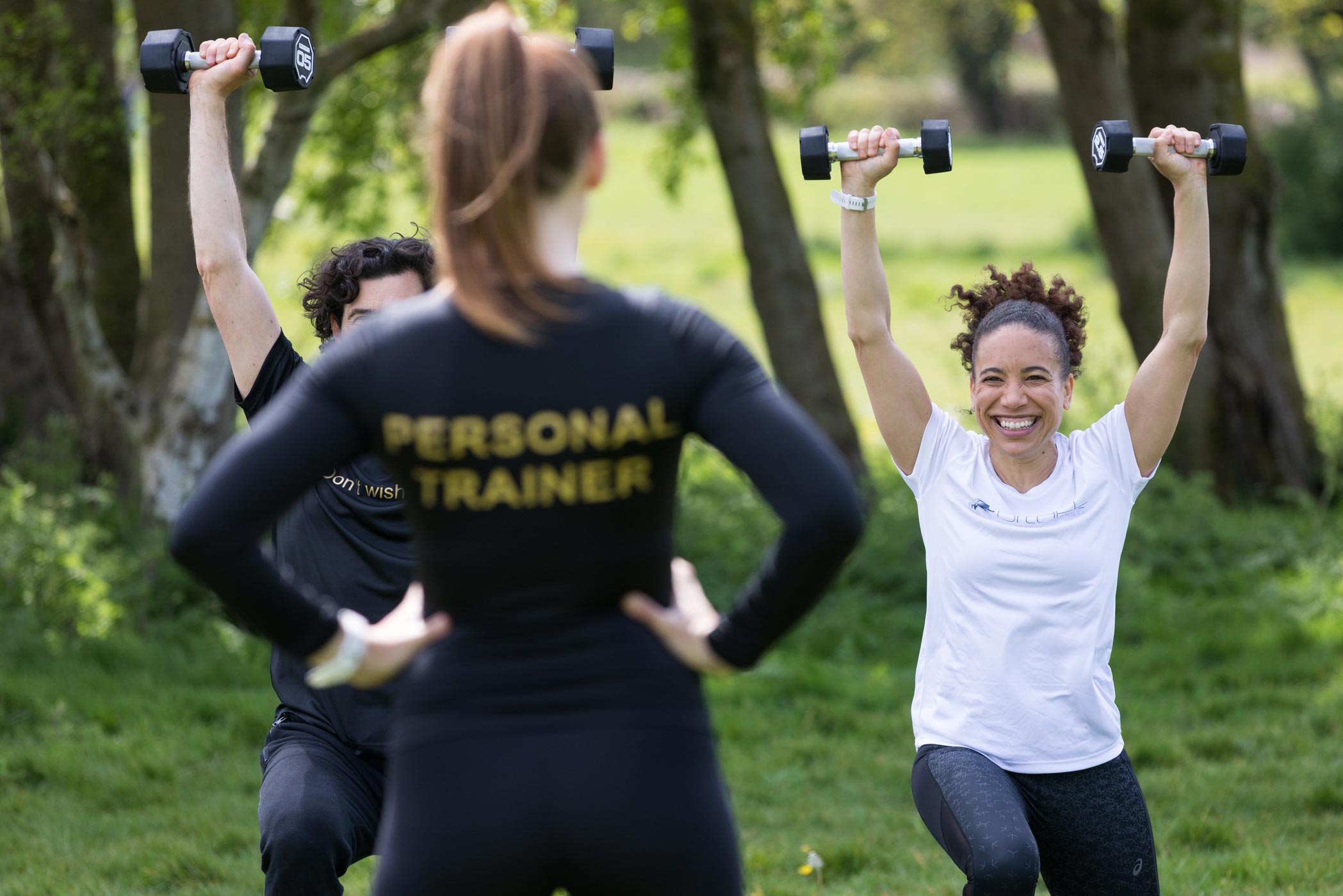A personal trainer watches her clients in the park whilst being photographed