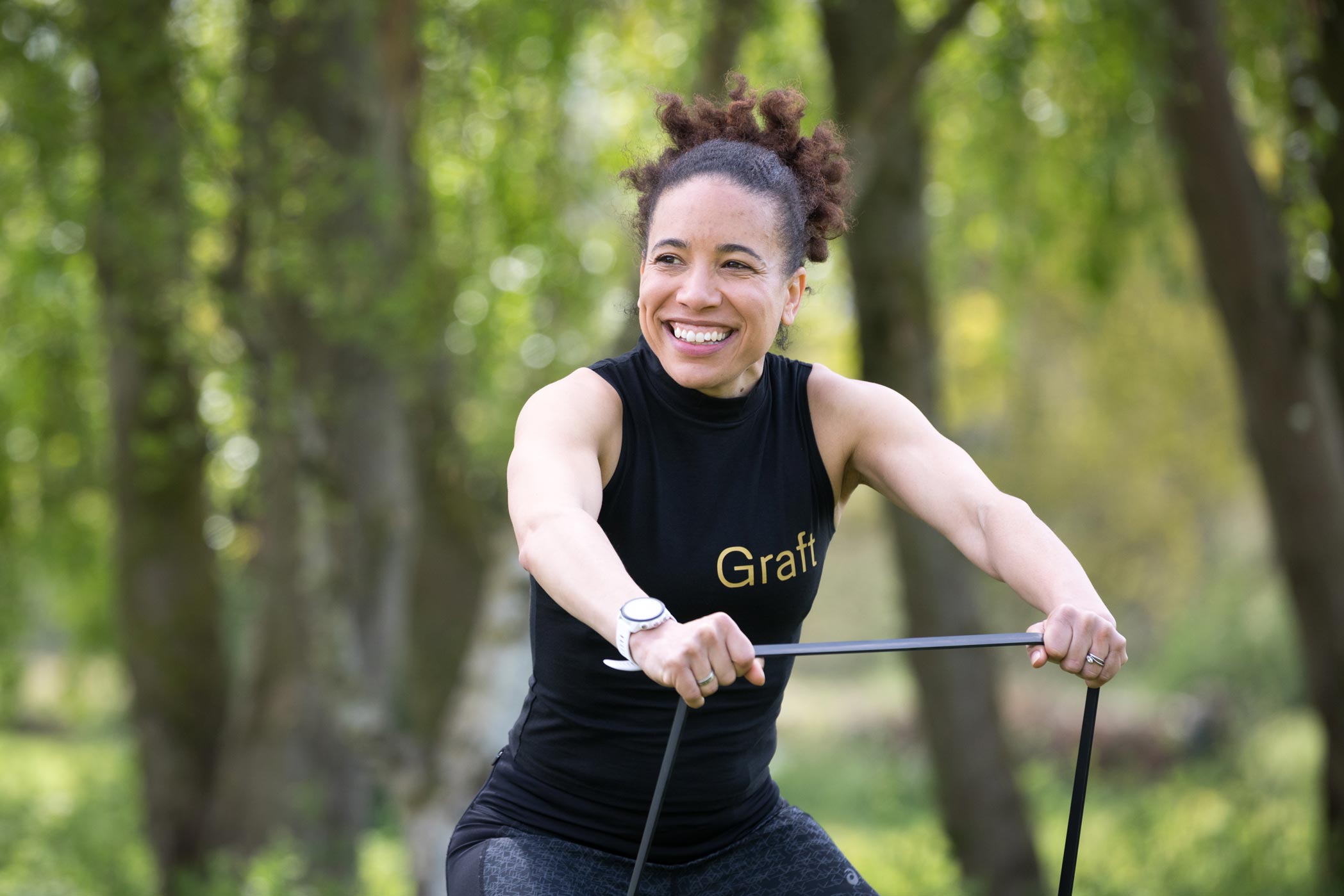 A smiling woman exercies in the park for a fitness brand photo shoot