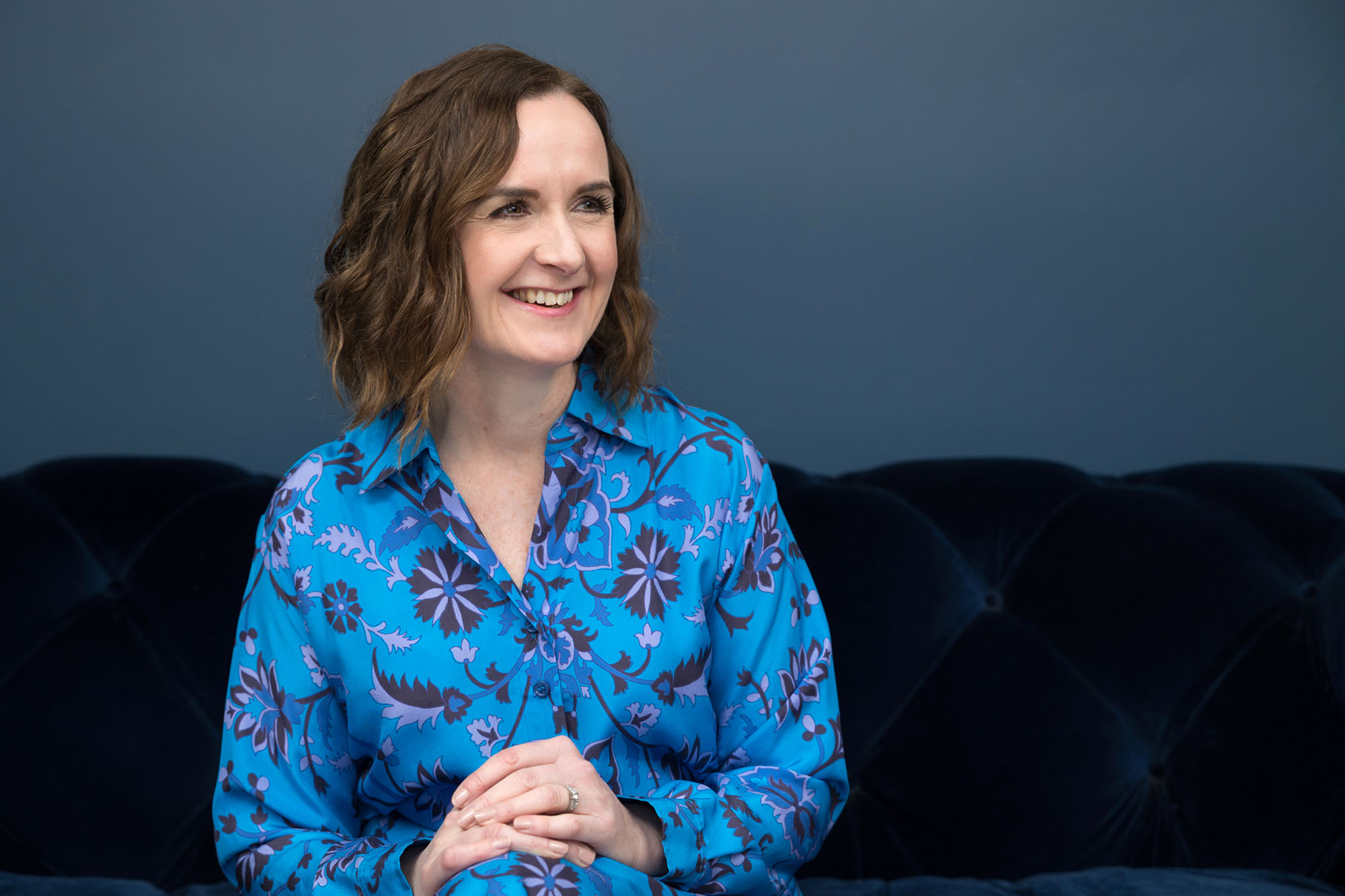 A smiling woman sitting in front of a blue wall during her Croydon personal branding photography shoot