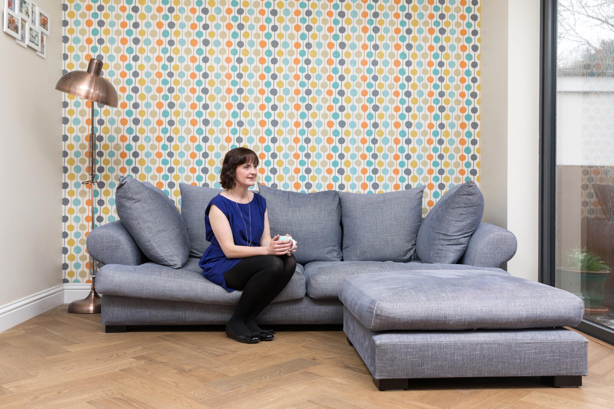 A woman sits on a sofa in front of a spotty wall during her Croydon personal brand photography shoot
