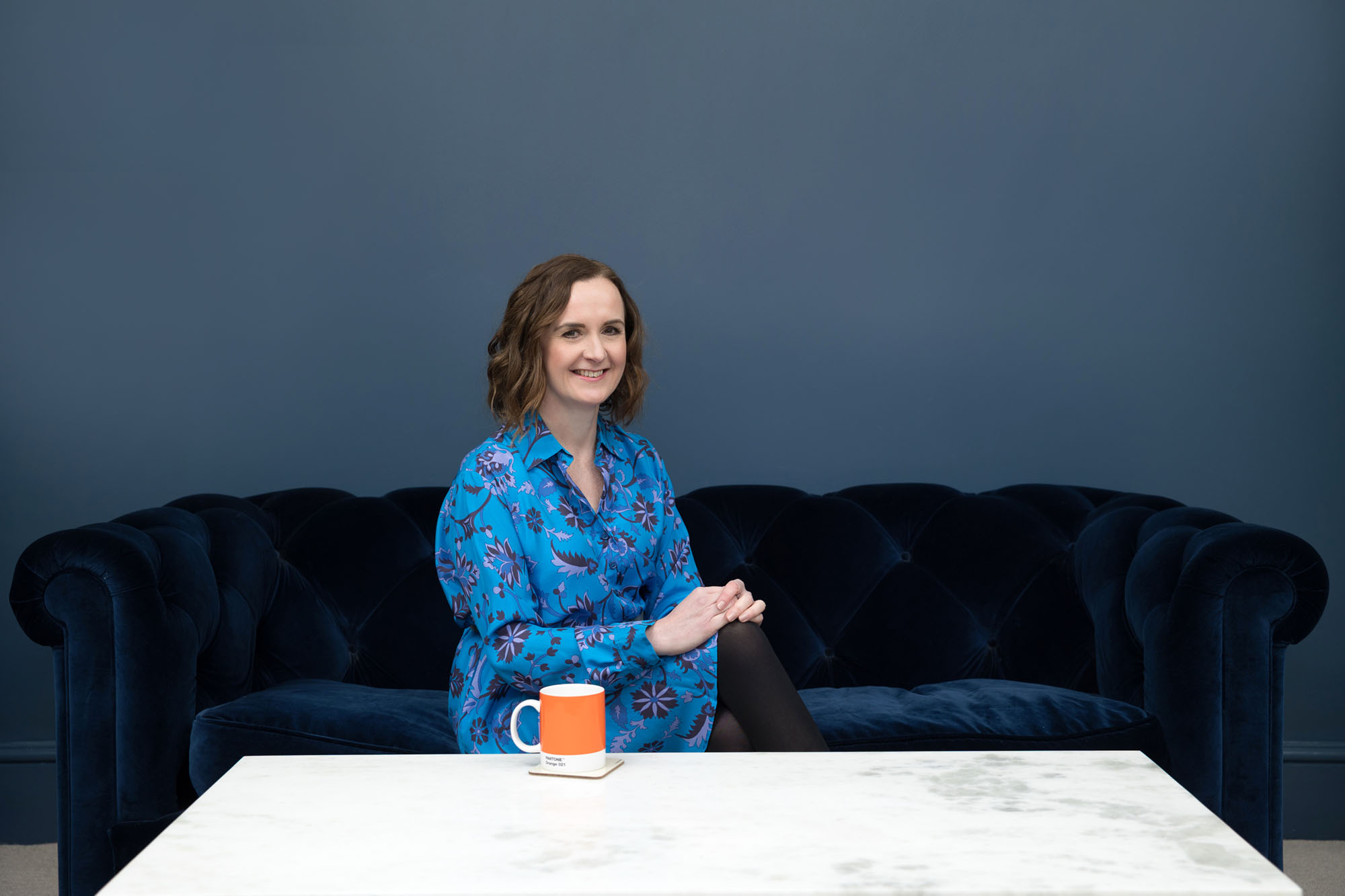 Personal branding photography in Croydon, London & Surrey. A woman sits on a blue sofa in front of a blue wall.