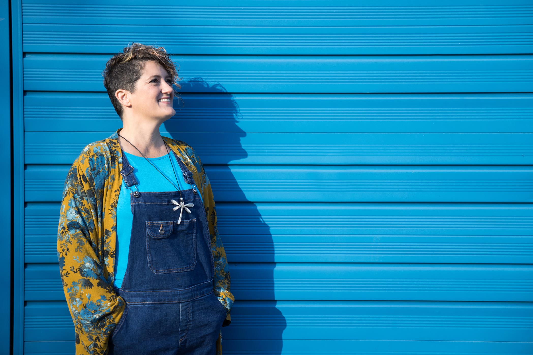 Personal branding photography in Croydon, Surrey. A woman stands in the sunshine in front of a blue wall.