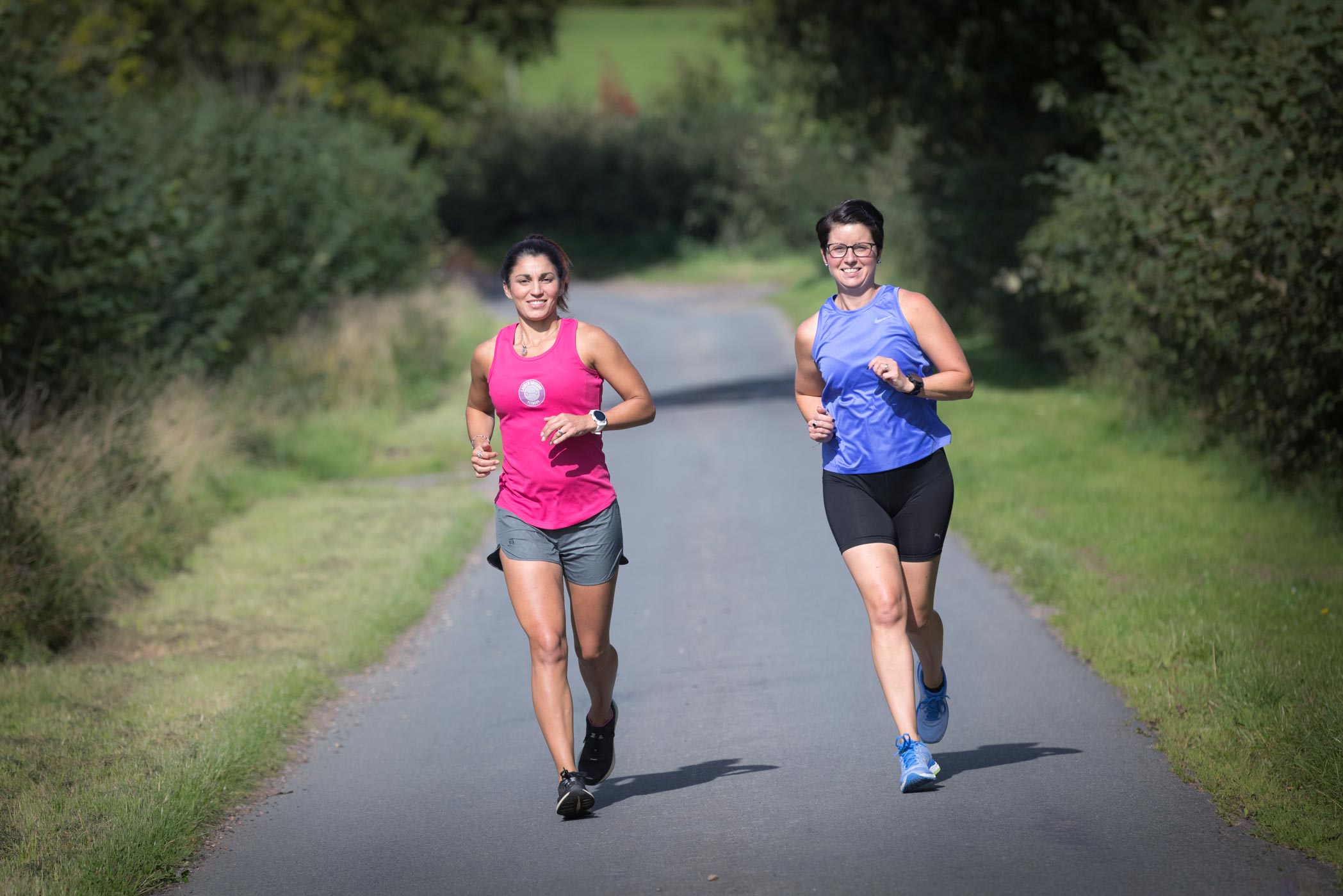 A running coach runs with her client along a country road during a health & fitness personal branding photography shoot in Warrickshire