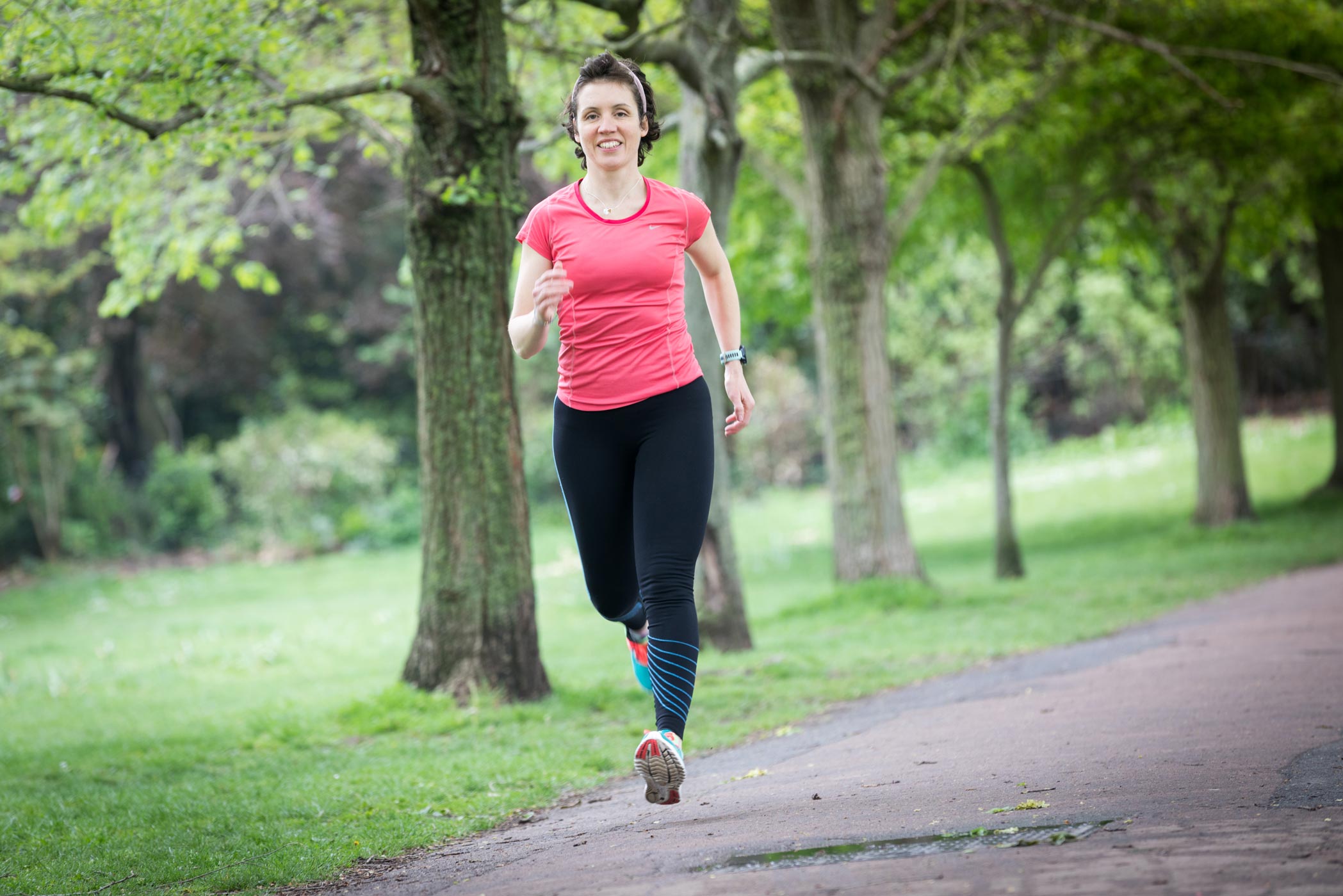 A female personal trainer runs in the park during a fitness personal branding photo shoot in London