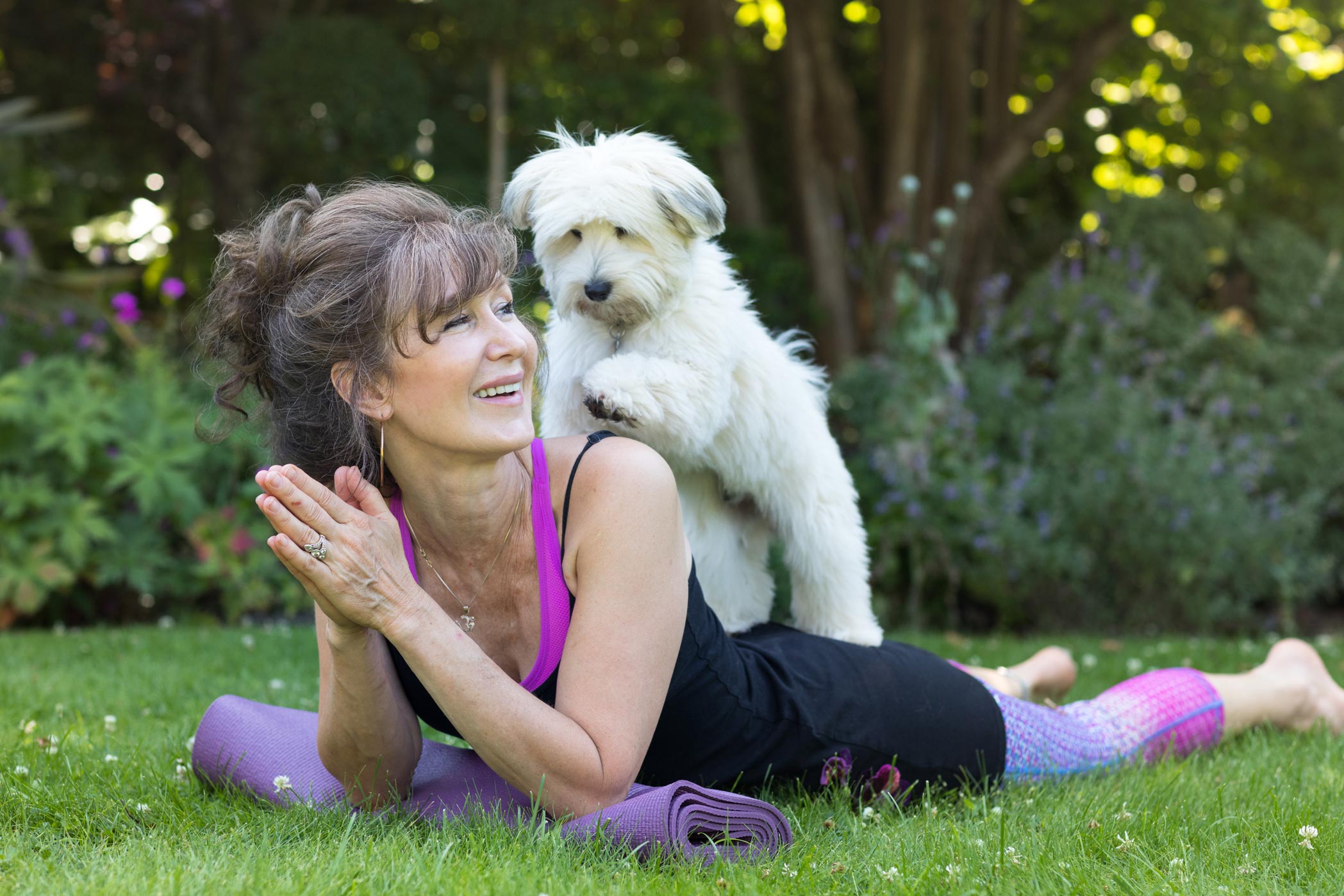 A dog climbs on the back of a yoga teacher as she lies on the mat during her practice at her health & fitness personal branding photography shoot in Croydon, London