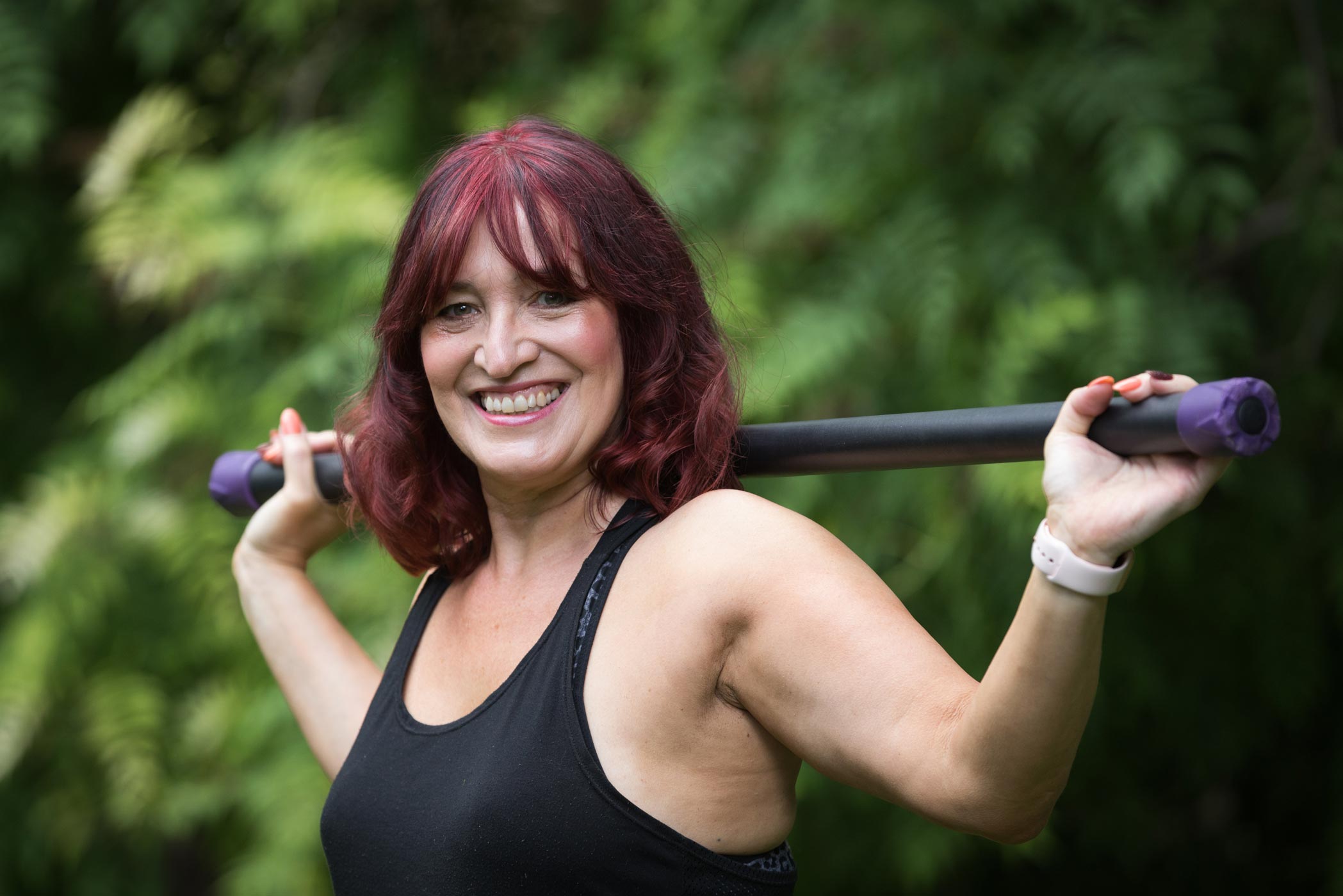 A female personal trainer holds a bar whilst posing for a photo as part of her health & fitness personal branding photography shoot in Croydon, London