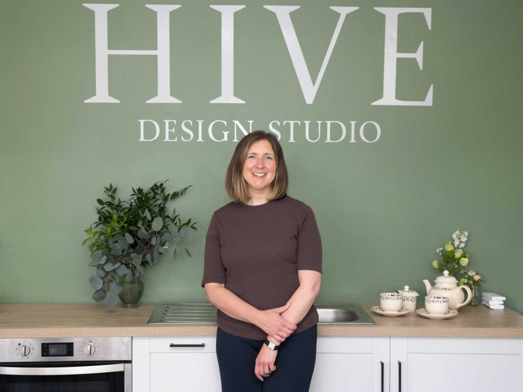 Brand photography at Hive Design Studio in Croydon. The business owner stands in front of a green wall with the brand logo on it.