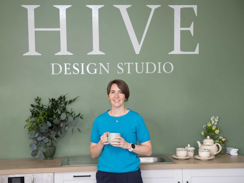 Brand photography at Hive Design Studio in Croydon. The business owner stands in front of a green wall with the brand logo on it.