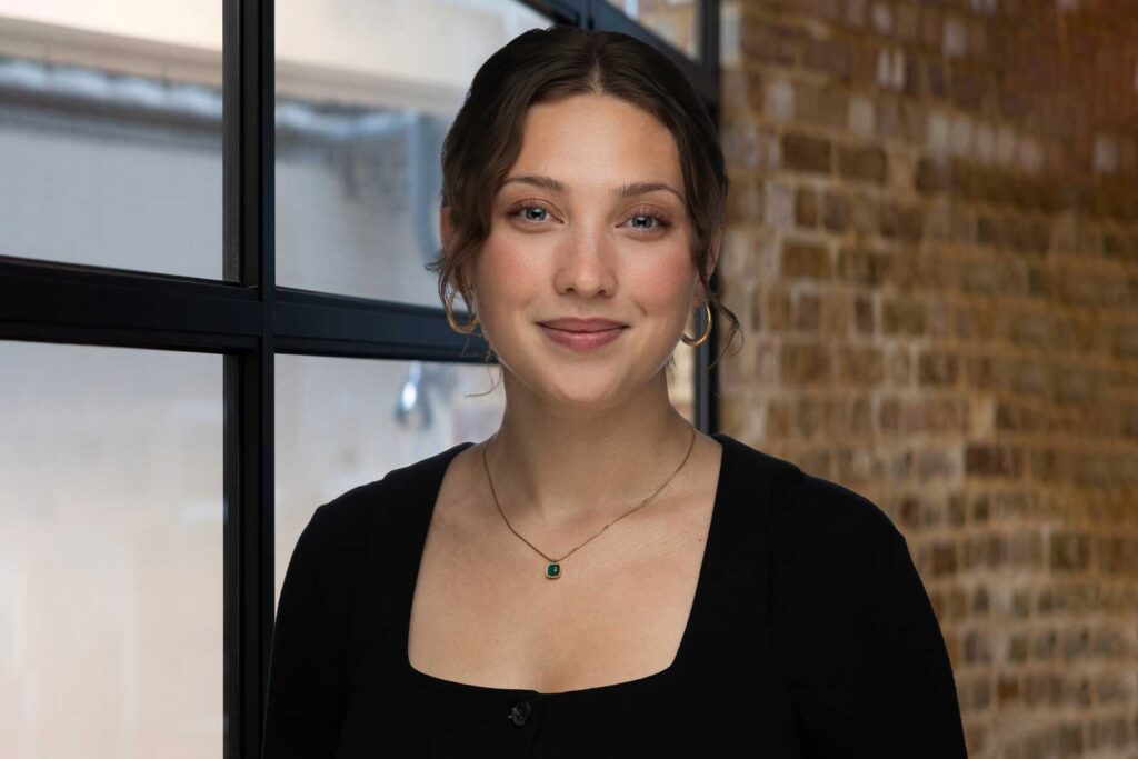 A smiling woman stands in front of a brick wall for her professional headshot photo in London