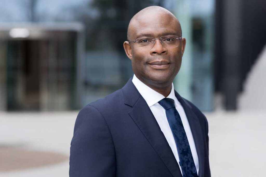 Corporate headshot photographer in London a business man wearing glasses in a dark blue suit in front of a reflective glass building